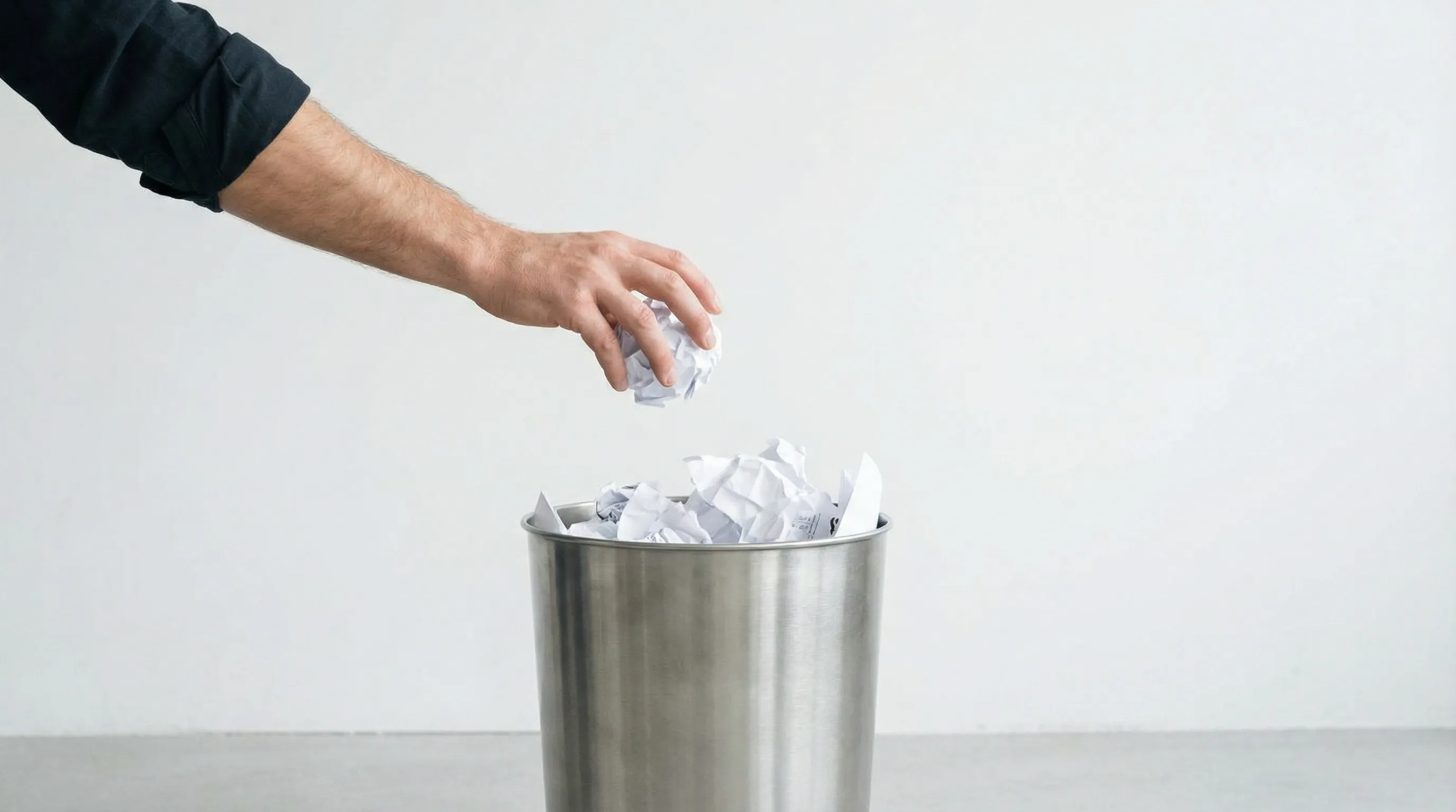 A photo of a hand throwing a piece of paper into the trash